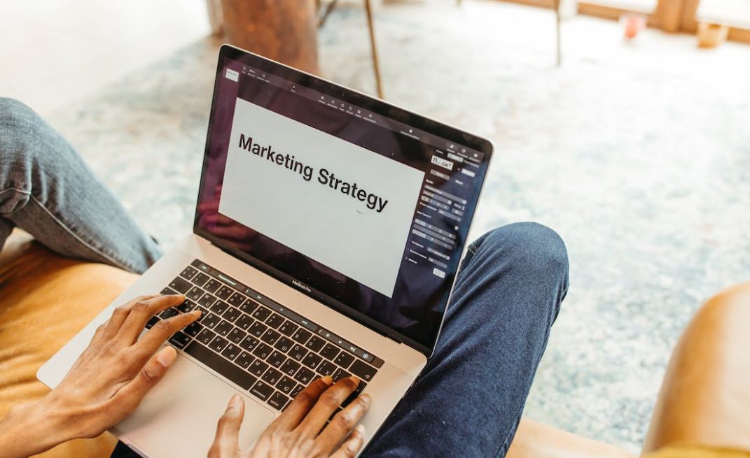 Een persoon die een laptop gebruikt met het woord marketingstrategie erop, specifiek gericht op e-mailmarketing.