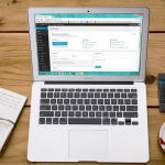 Een laptop staat op een houten tafel naast een kopje koffie en een notitieboekje, terwijl de gebruiker werkt aan het maken van zijn WordPress-website.
