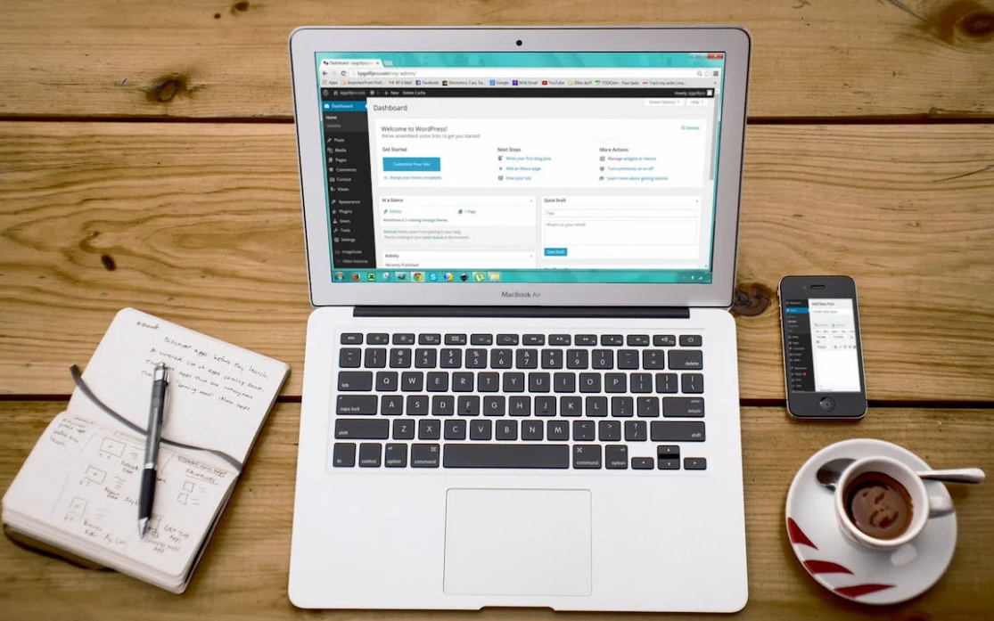 Een laptop staat op een houten tafel naast een kopje koffie en een notitieboekje, terwijl de gebruiker werkt aan het maken van zijn WordPress-website.