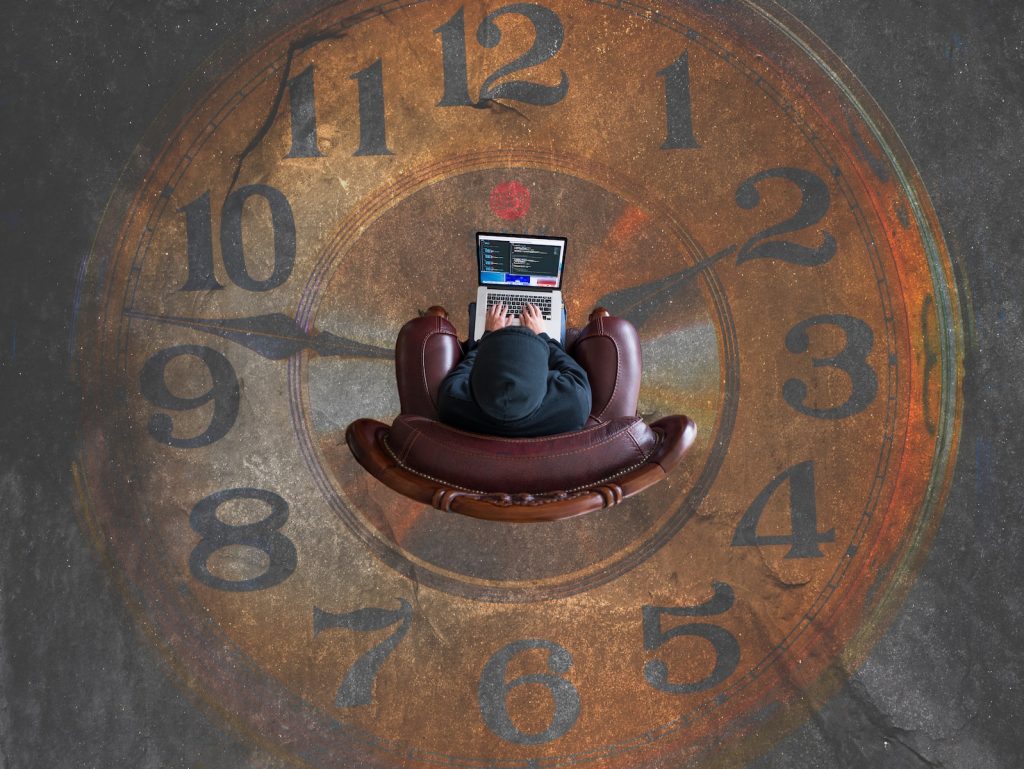 Een inhoudseditor zit in een stoel met een laptop voor een klok.